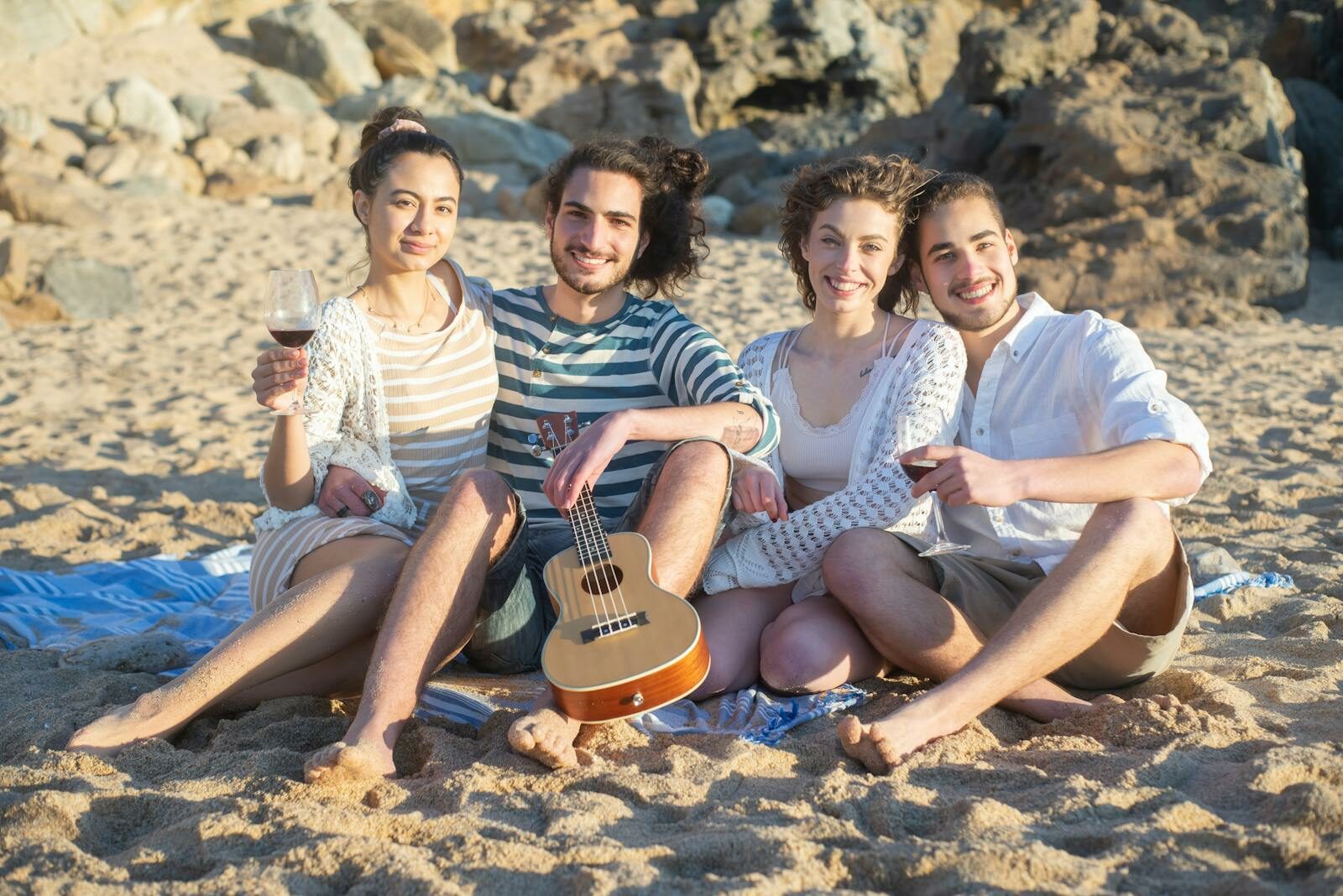 Group of friends sitting on beach with a ukulele and wine, enjoying a leisure day.