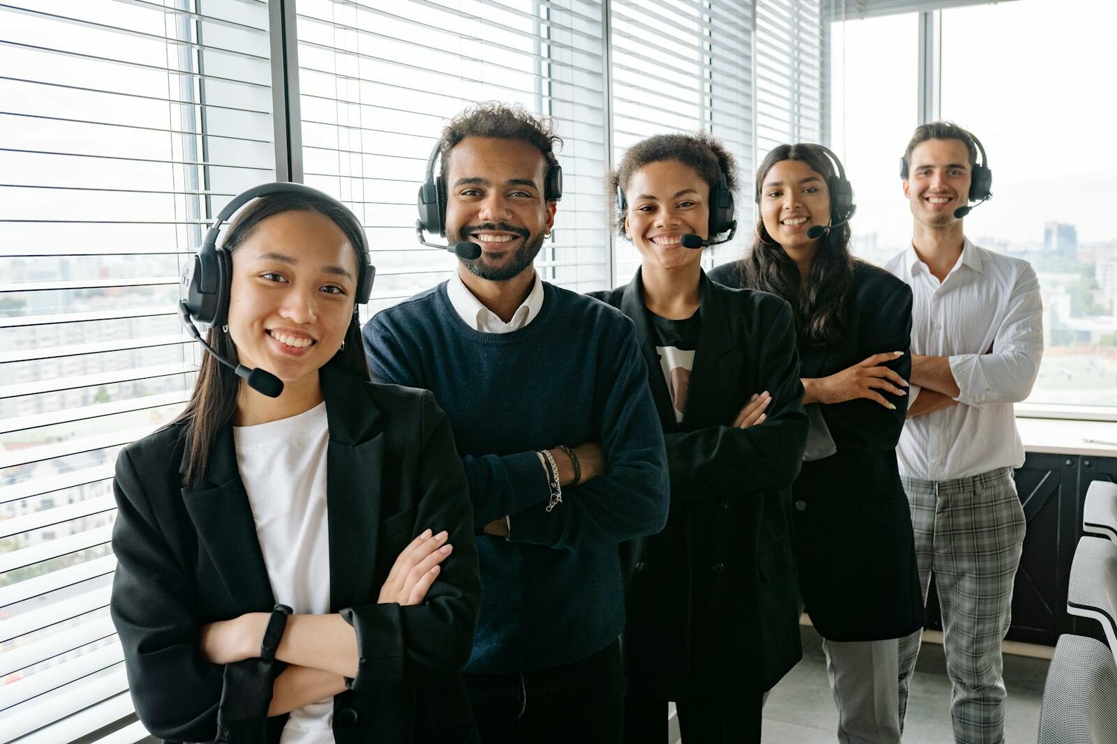 A cheerful, diverse team with headsets posing in a bright office environment.